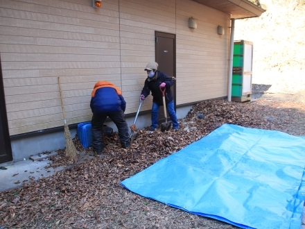 建物の裏側に溜まった落ち葉を除去するボランティア
